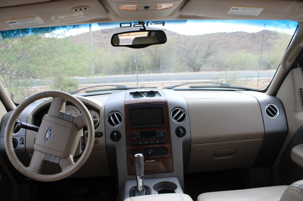 Interior view of a Ford vehicle, showing the dashboard, steering wheel, control panel, and windshield, with a backdrop of a mountainous landscape.